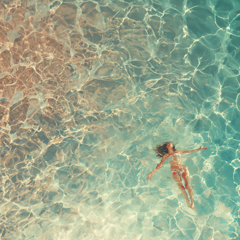 Mujer flotando en aguas cristalinas y turquesas, vista aérea.